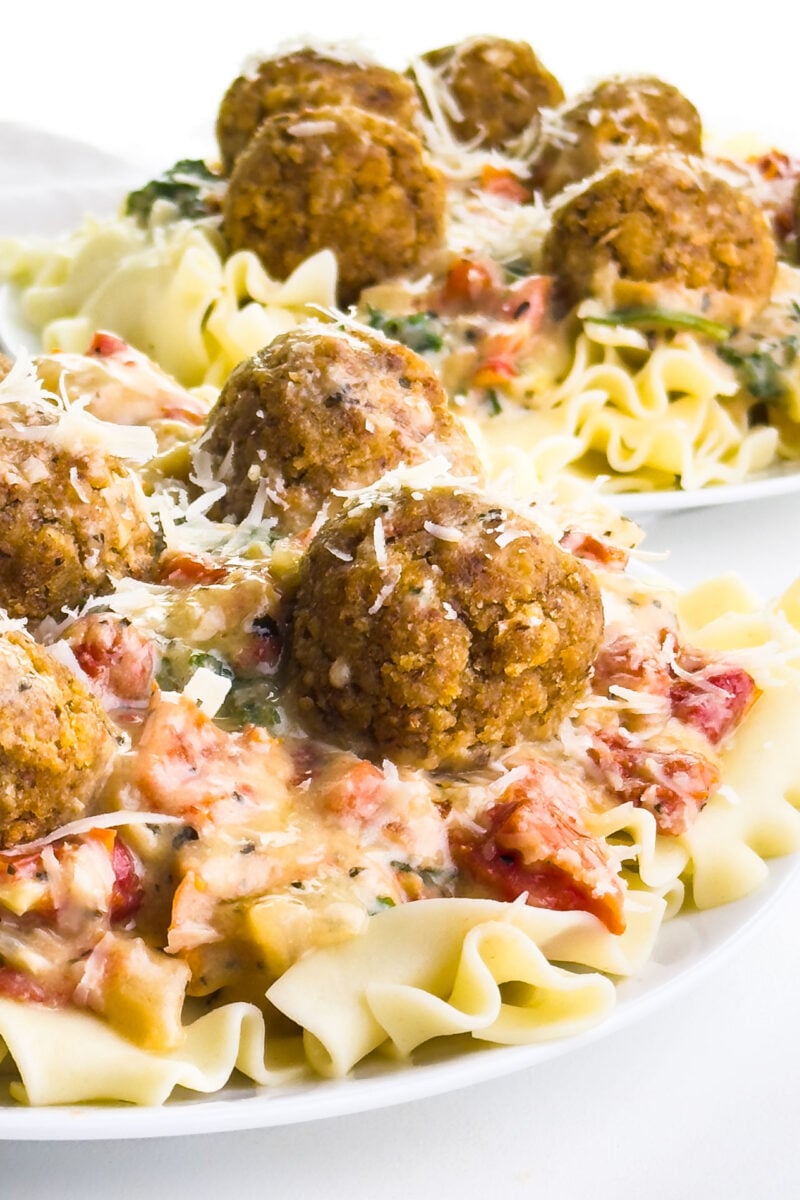 Vegan meatballs are served over a sauce and noodles on a plate.