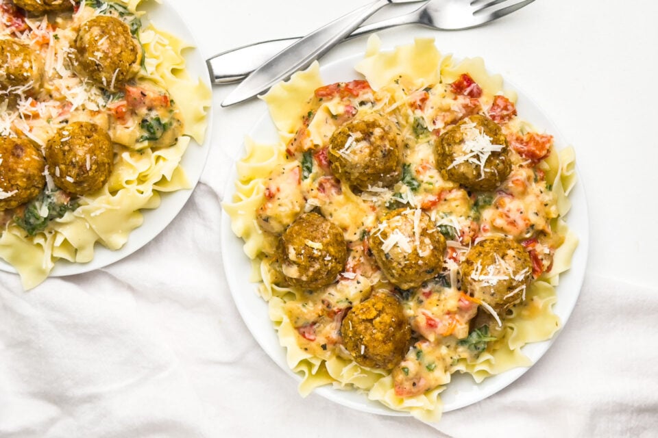 Looking down on two plates with noodles, vegan marry-me sauce, and meatballs.