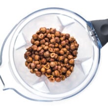 Looking down on a blender jar filled with roasted, shelled hazelnuts.