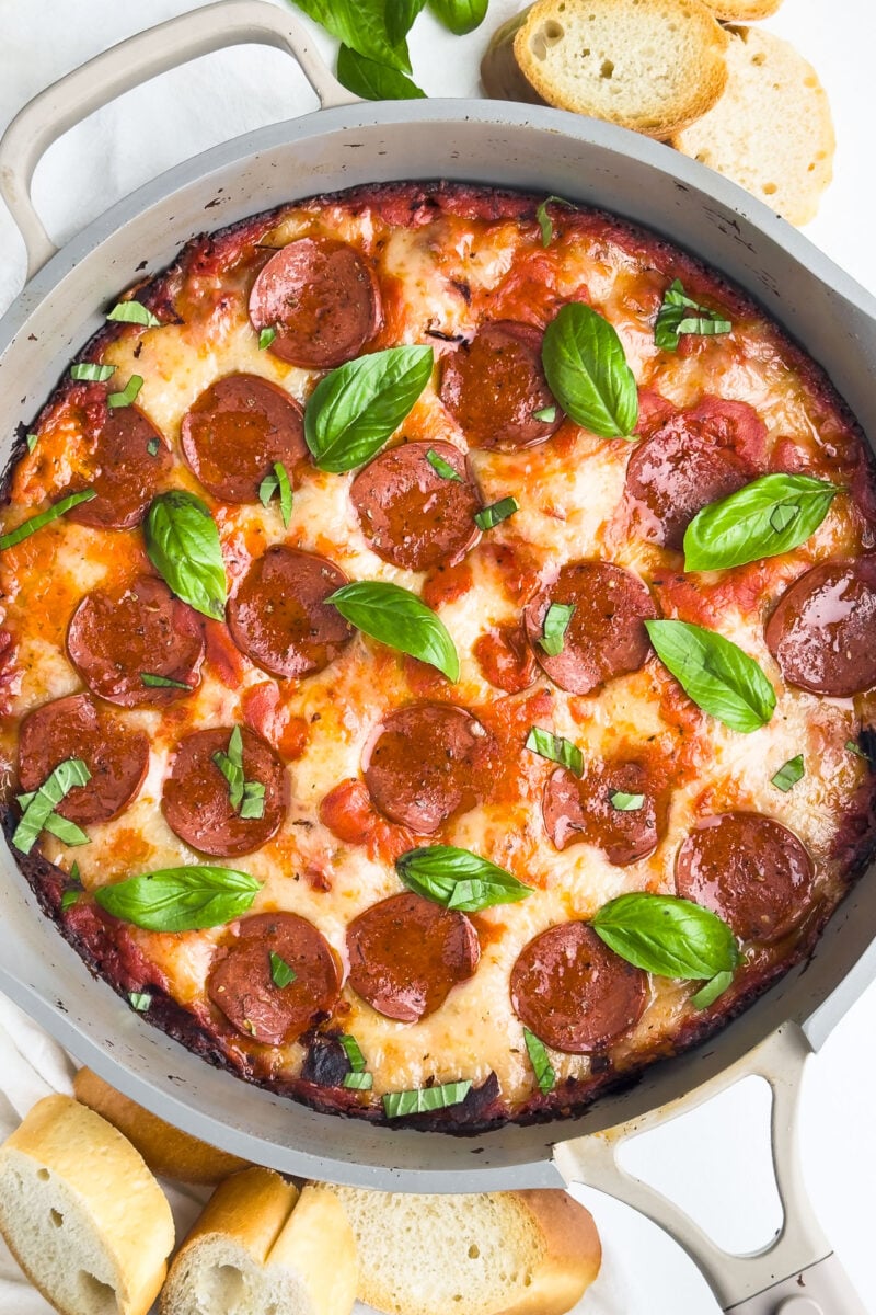 A skillet is filled with pizza dip, including pepperoni and basil on top.