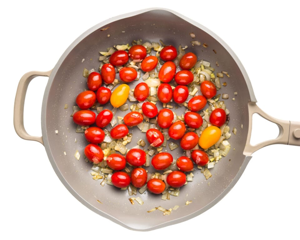 Cherry tomatoes are cooking in olive oil in a skillet.