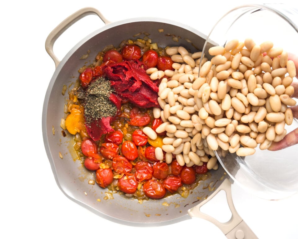 Beans are added to a skillet with tomatoes and other ingredients.