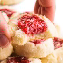 A hand holds a raspberry coconut thumbprint cookie with a bite taken out.