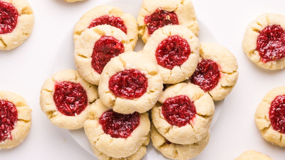 Looking down on a plate of raspberry thumbprint cookies with more cookies sitting around the plate.