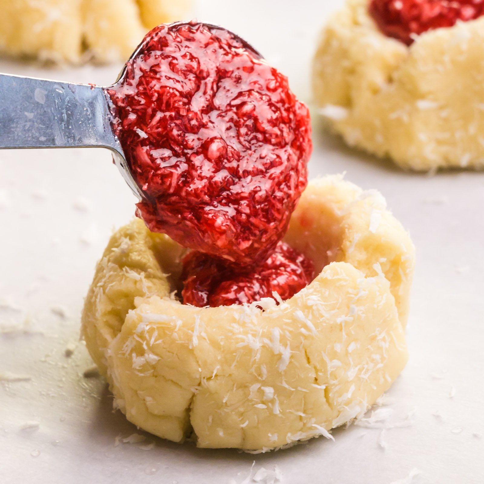 Raspberry jam is being added to a thumbprint cookie.