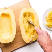 The insides of a spaghetti squash are being scraped of with a spoon.