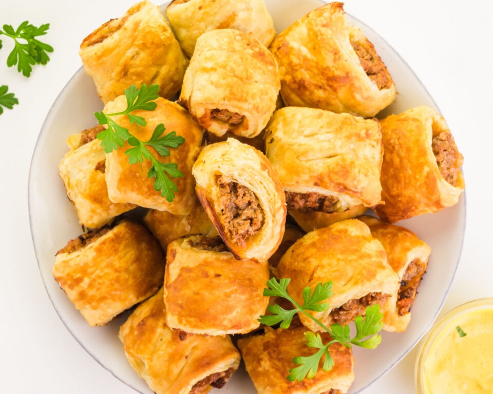 Looking down on a plate of vegan sauce rolls sitting next to a dipping sauce and herbs.