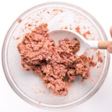 A hand stirs vegan sausage mixture in a bowl.