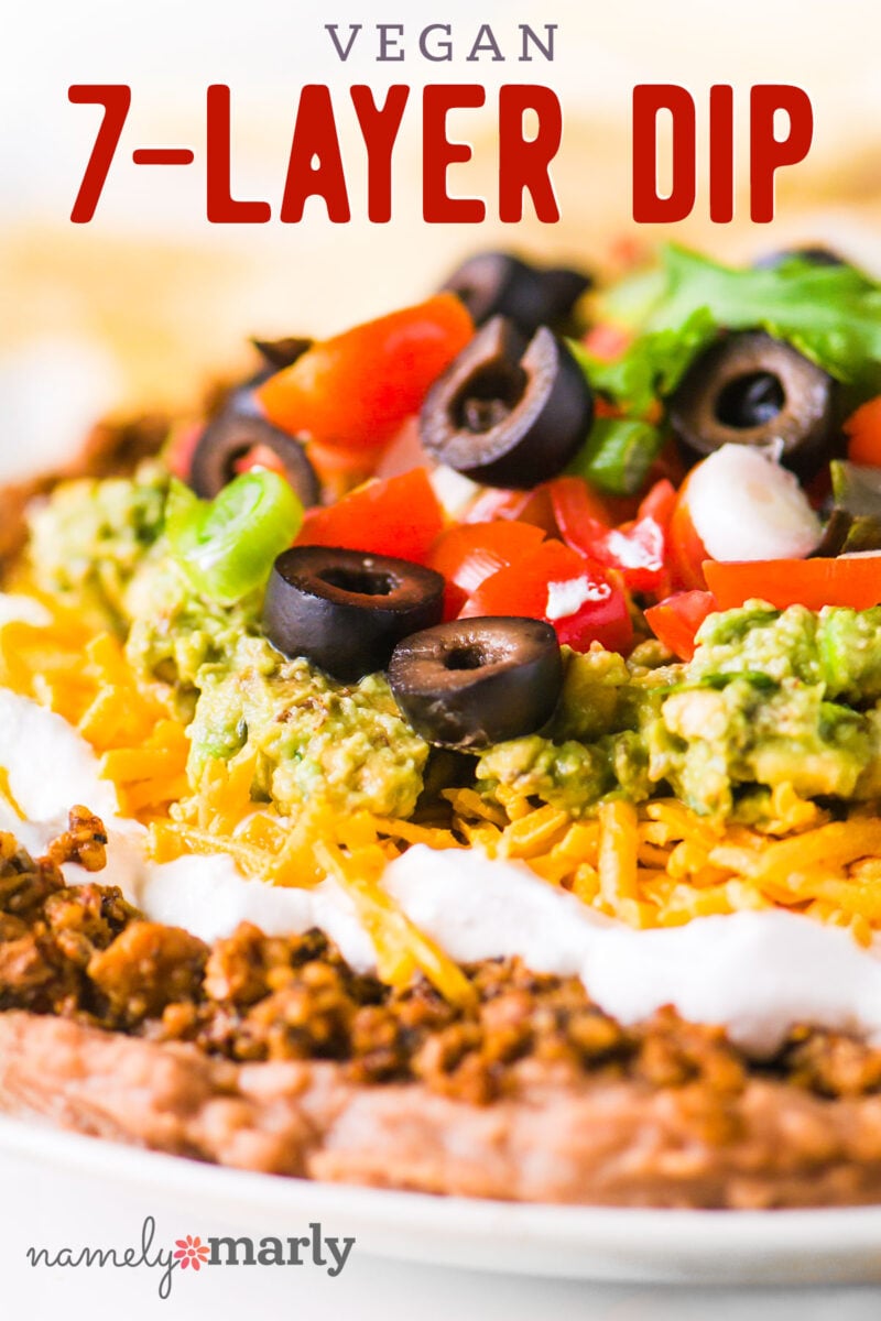 Close up image of vegan meat, cheese, sour cream, olives, guacamole and more. The text reads, Vegan 7-Layer Dip