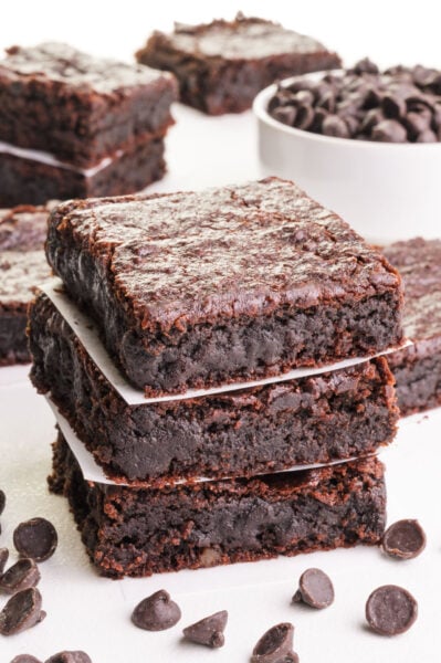 A stack of chickpea brownies has chocolate chips in front and in a bowl behind it.