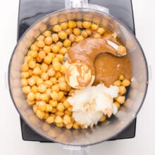 A food processor is full of ingredients like chickpeas, maple syrup, and coconut oil.