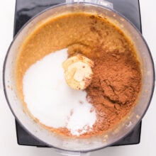 A food processor is full of ingredients like a mixed chickpea batter, cocoa powder, and sugar.