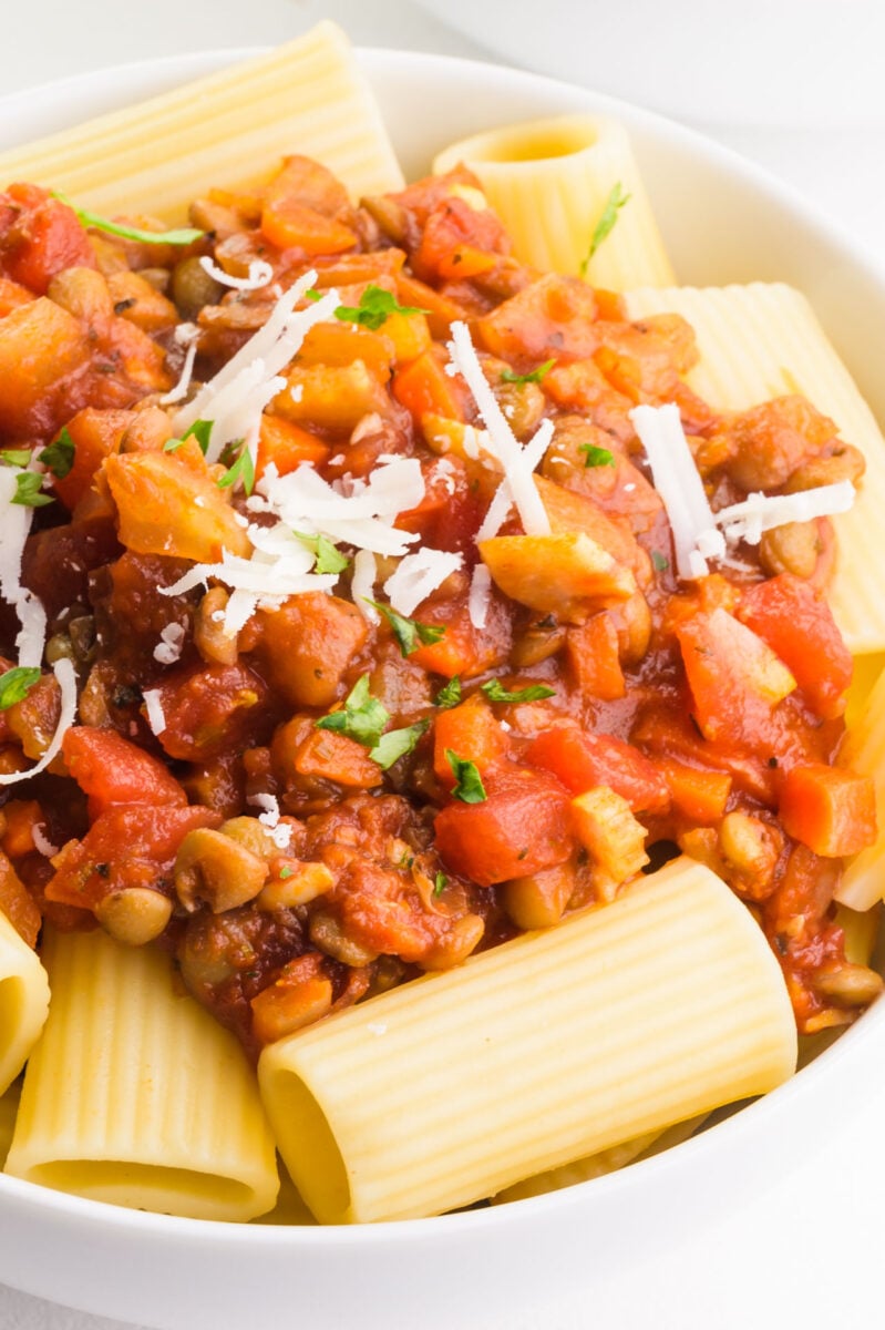 A plateful of lentil bolognese is topped with grated vegan parmesan cheese.
