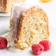 A slice of lemon poppyseed cake has raspberries next to it.