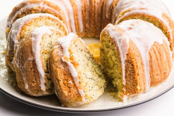 A bundt cake on a pate has slices taken out and glaze on top.