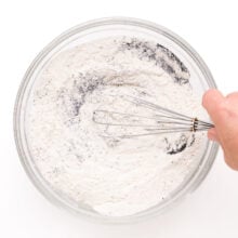 A flour mixture is being whisked int a mixing bowl.
