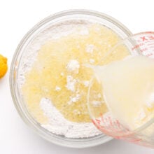 A wet mixture is being poured into a mixing bowl with flour ingredients.