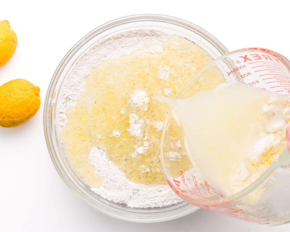 A wet mixture is being poured into a mixing bowl with flour ingredients.