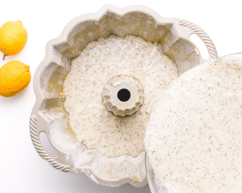 Cake batter is being poured into a bundt pan next two fresh lemons.