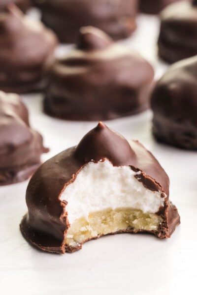 A closeup of vegan mallomars, one with a bite taken out revealing lots of marshmallow creme under a chocolate coating.