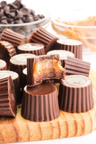 Several vegan rolos are on a cutting board, one with a bite taken out revealing caramel inside the chocolate candy.