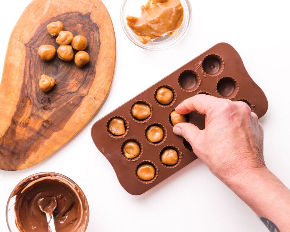 Caramel balls are being added to candy molds filled with chilled chocolate.