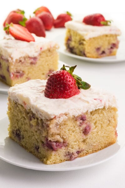 A slice of vegan strawberry cake on a plate has a fresh strawberry on top.