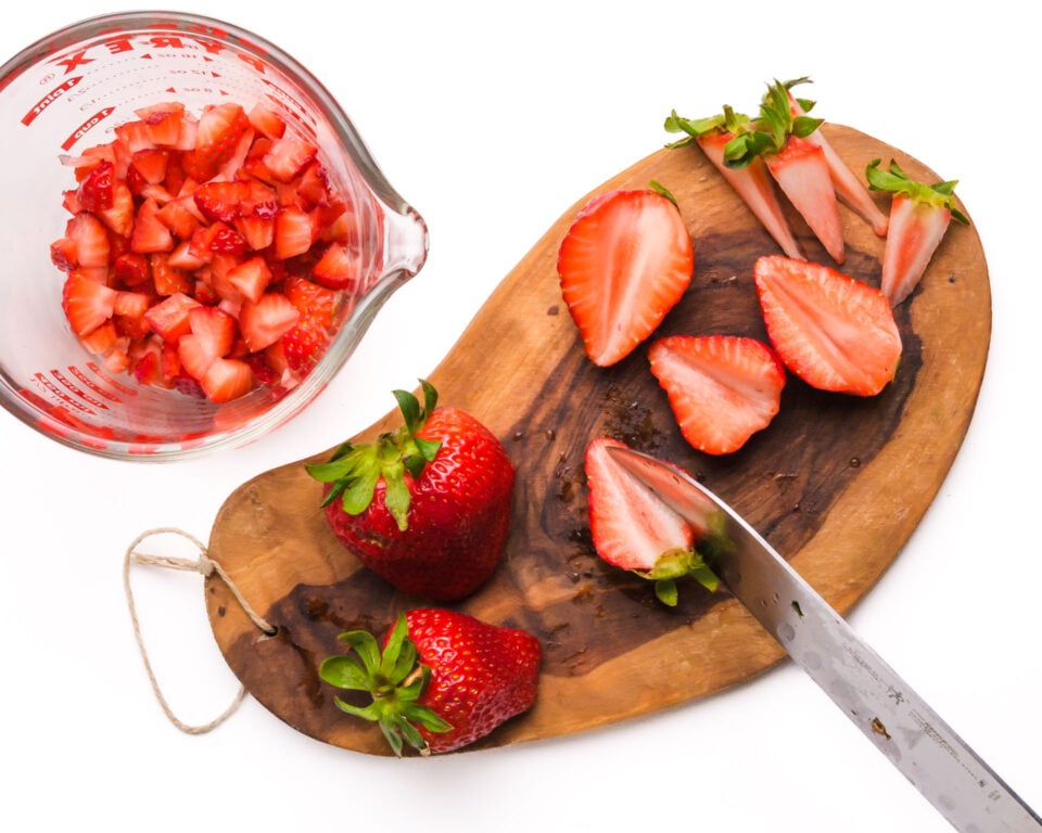 A knife is cutting strawberries on a wooden cutting board.