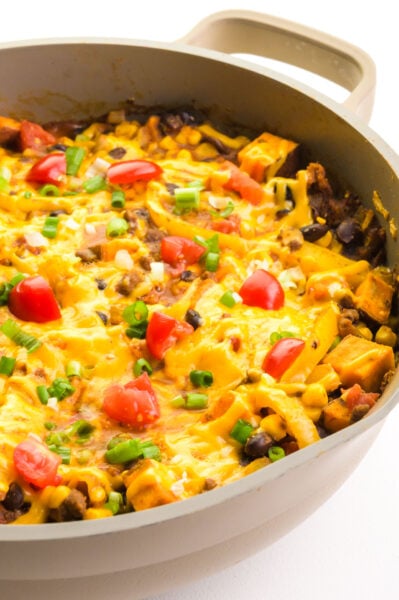Looking into a pan of sweet potato taco skillet with melted cheese, diced tomatoes, and chopped green onions on top.