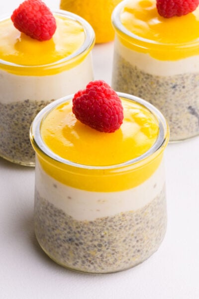 Three glass serving dishes hold chia pudding with lemon topping and raspberries on top.