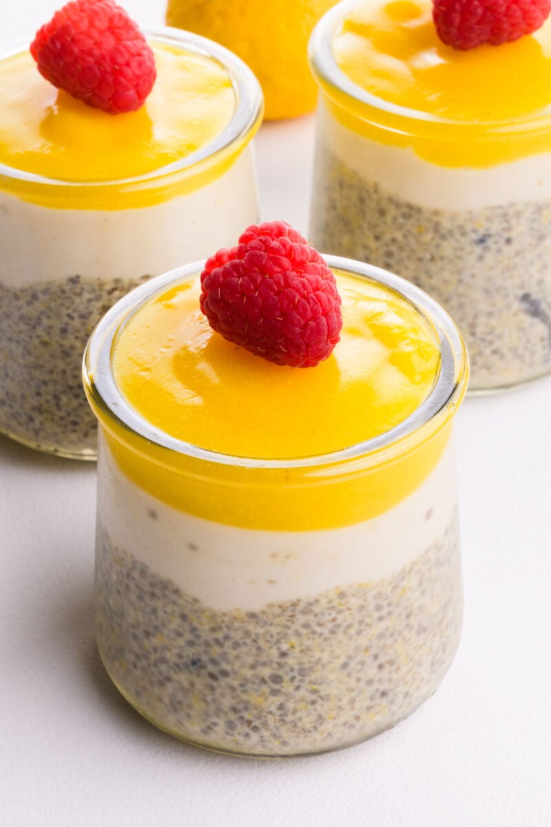 Three glass serving dishes hold chia pudding with lemon topping and raspberries on top.