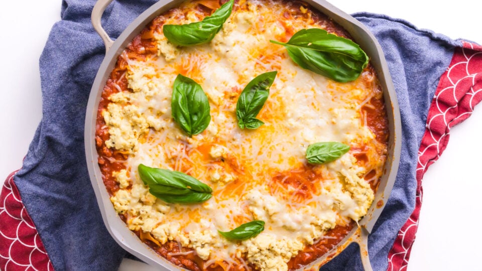 Looking down on a skillet full of a quick lasagna mixture topped with cheese and herbs.