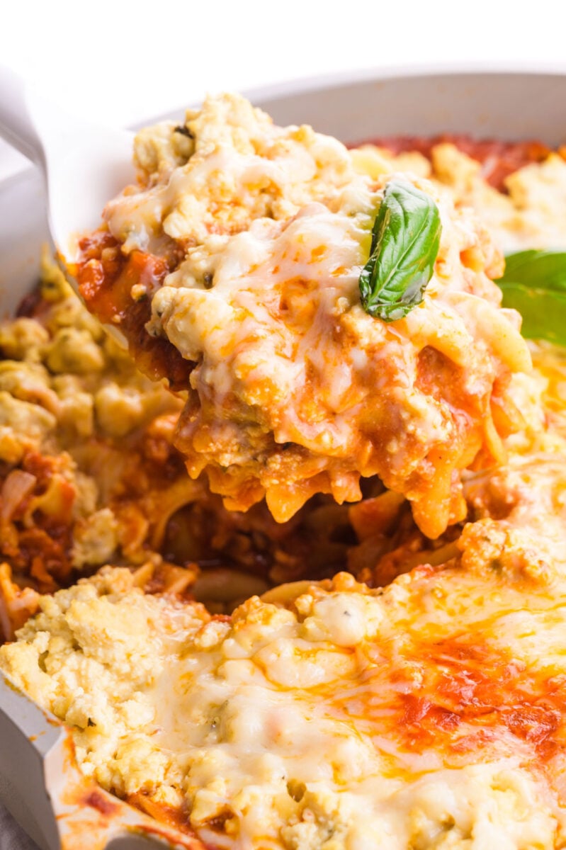 A spoonful of vegan skillet lasagna is topped with melted cheese and green herbs.