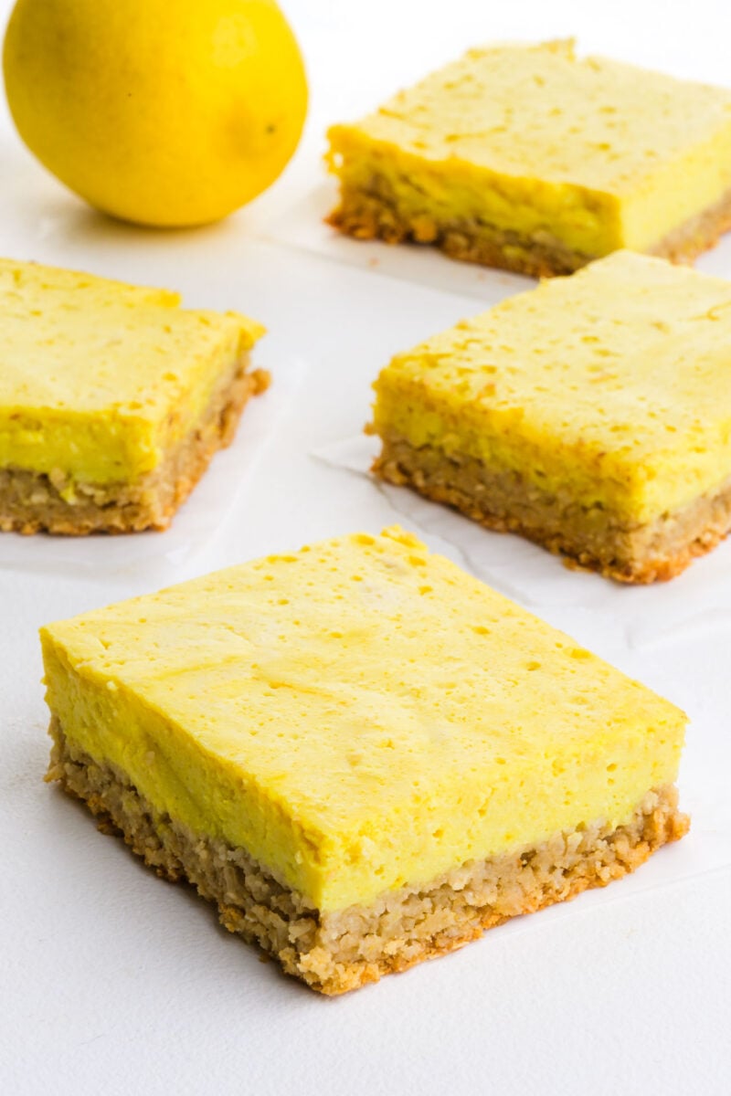 Several lemon dessert bars on a white table with a fresh lemon.