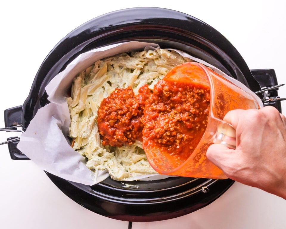 Red sauce is being poured over pasta in slow cooker.