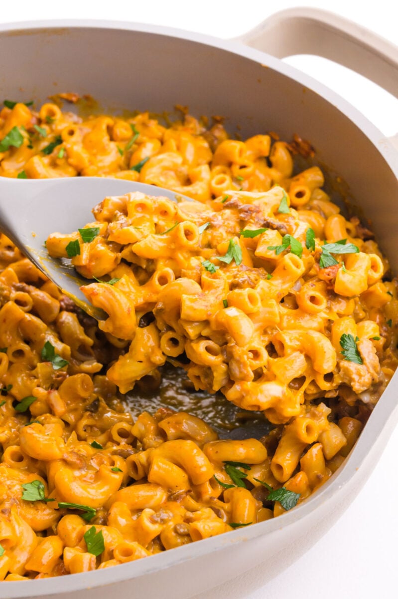 A spatula dishes out a serving of cheesy macaroni hamburger helper type dish from a skillet.