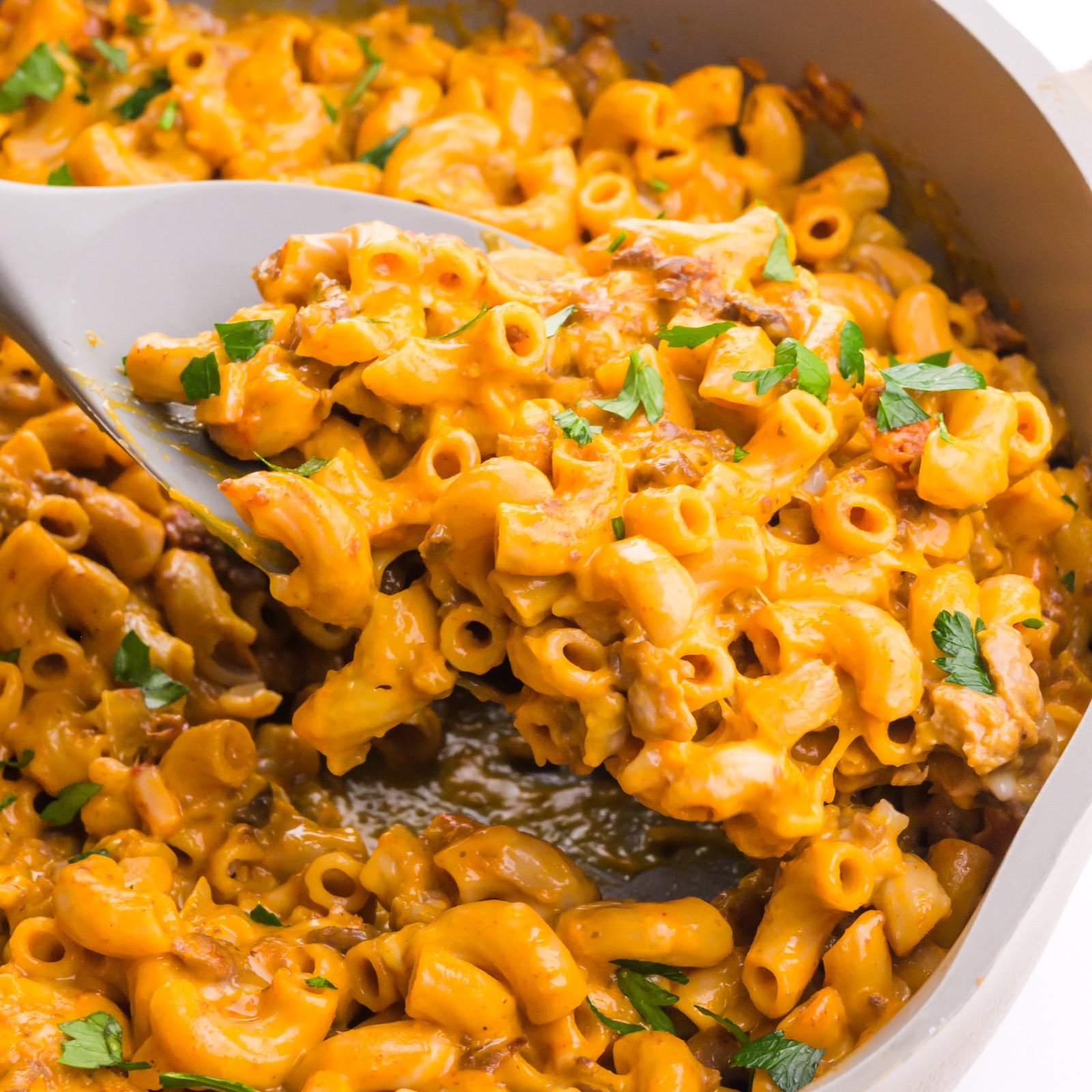 A spatula dishes out a helping of cheesy macaroni from a skillet.