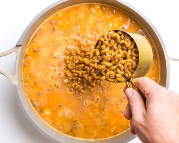 Pasta is being poured into a skillet with a cheesy broth.