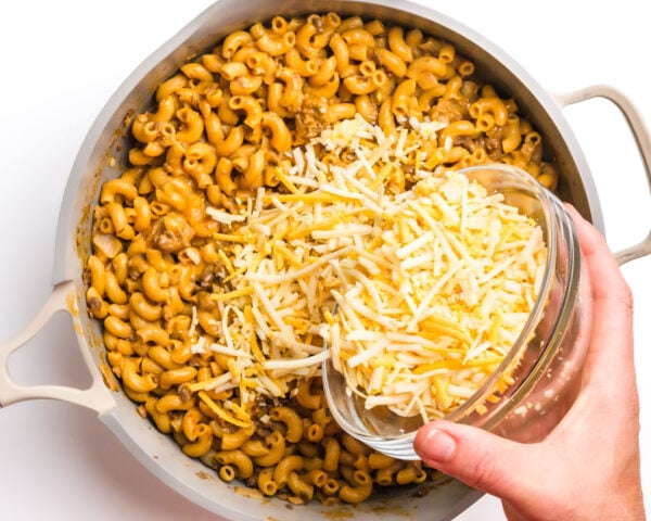 Cheese is being poured into a skillet with a macaroni mixture.