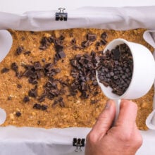 Chocolate chips are being spread over a crust in a baking dish.