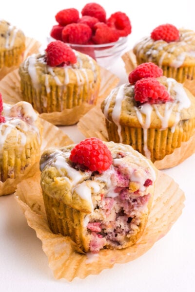 Several raspberry banana muffins on a table and one has a bite taken out.