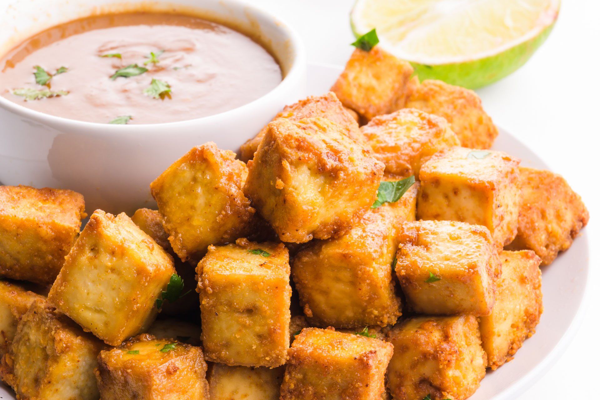 Crispy fried tofu on a plate next to a bowl of sauce.
