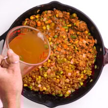 Broth is being poured into a skillet with vegetables and other ingredients.