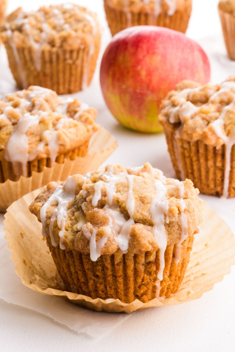 Several apple muffins are on a white table with a red apple.