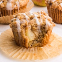An apple crumb muffin has vanilla drizzles on top and a bite taken out.
