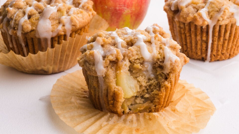 An apple muffins has a bite taken out revealing tender apple chunks inside.