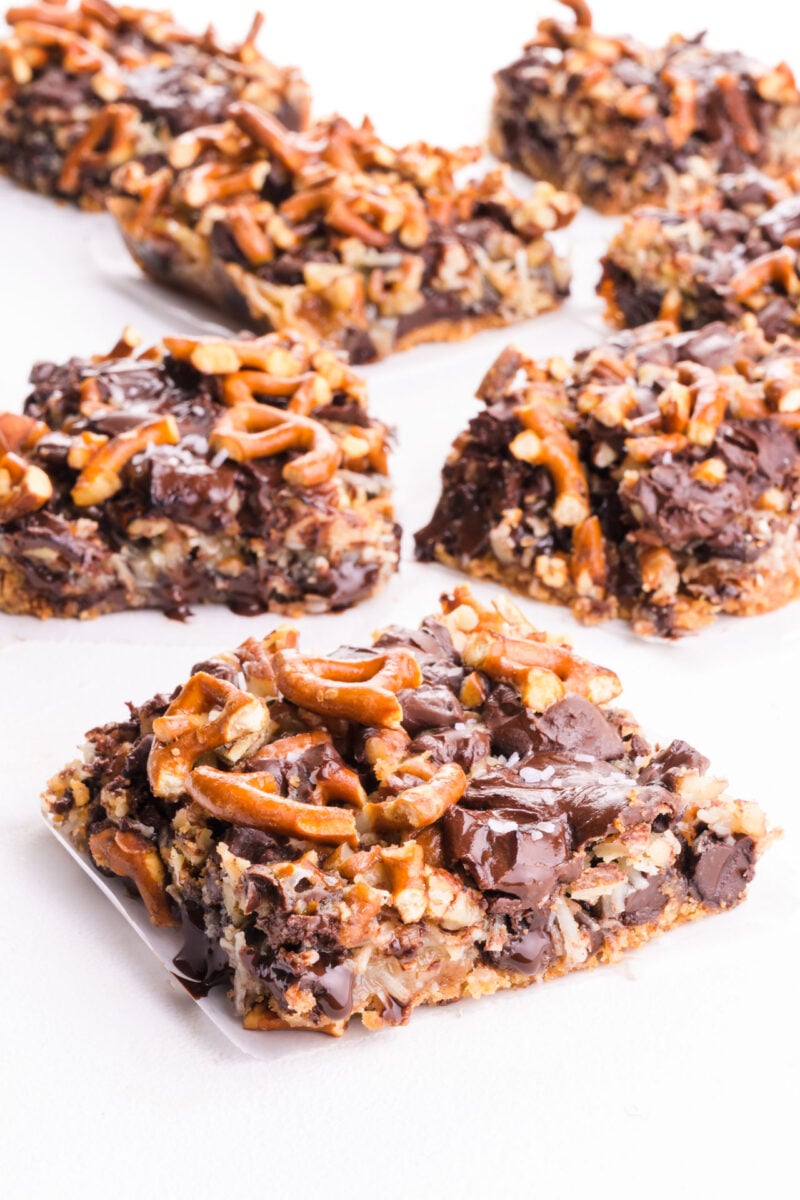 Several slices of vegan 7 layer bars infused with melty chocolate chips on a white table.