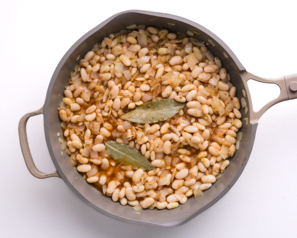 Looking down on a skillet with white beans and rice topped with bay leaves.