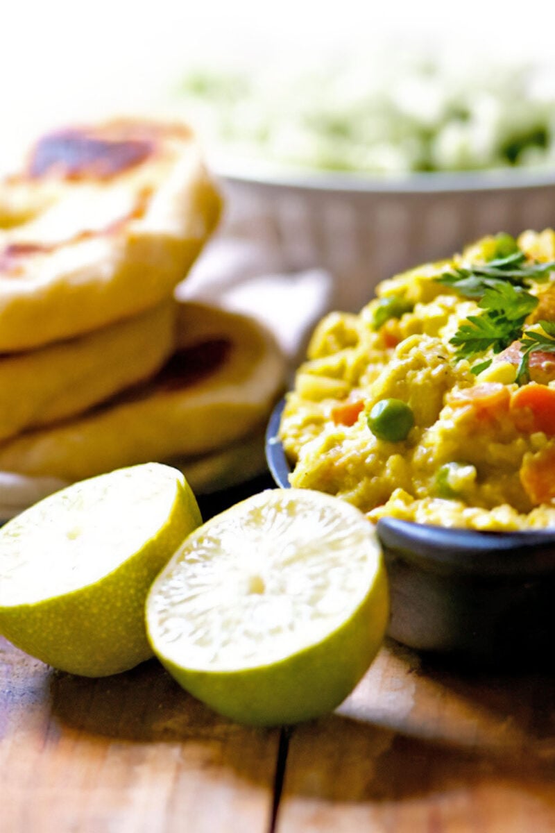 A serving dish full of chickpea curry sits next to naan bread and limes.