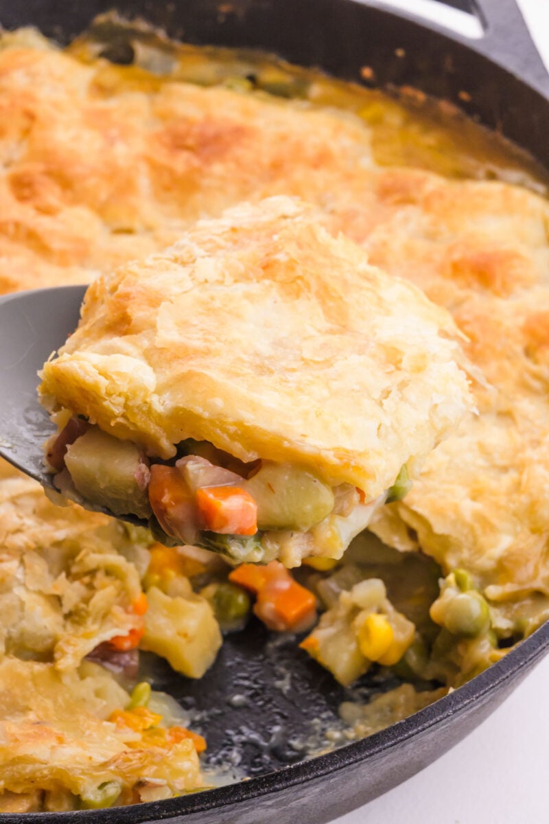 A serving of vegan chicken pot pie hovers over the skillet with the rest of the dish.